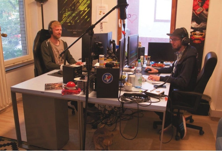 Broadcast Engineer Max Zelass an seinem Arbeitsplatz im Büro mit Editor Oliver Steffens und Jack-Russel-Dame Kimi. n AT WORK Rocket Beans TV